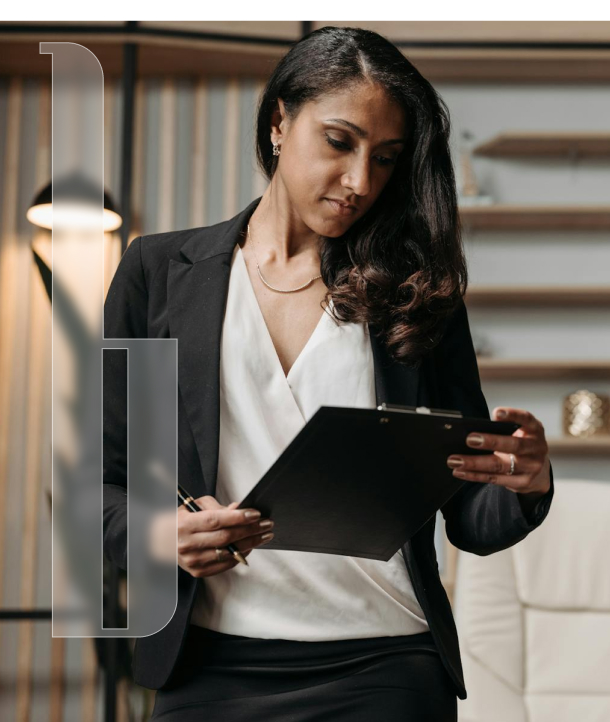 A woman in business attire holds a clipboard and pen, standing in a modern office setting with shelves and a lamp in the background.