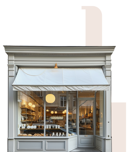 Street view of a bakery or café with a white awning, large glass windows displaying baked goods, and warm lighting inside.